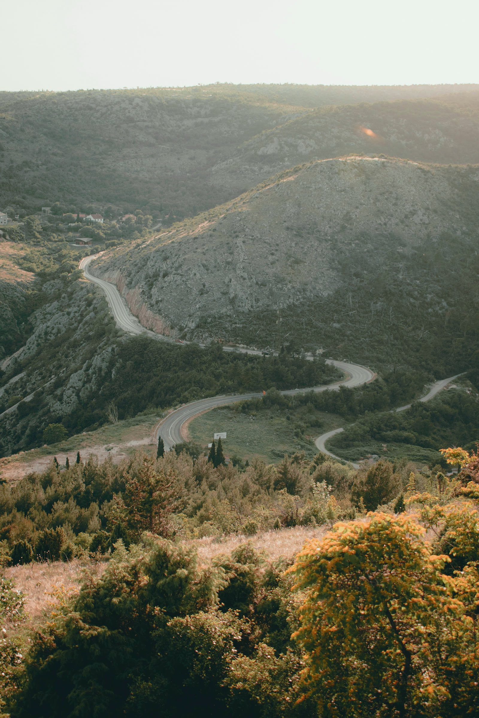 A road winding through karst hills in Herzegovina at golden hour.